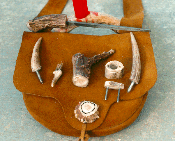 From top: candle stick, handled file, clothes hooks (left and right), pan brush (left center), open cap box (right center), and priming horn (middle). A button made from the base of the antler is sewn on the bottom of the pouch.